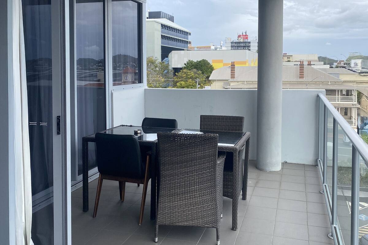 A balcony with a table and chairs, a glass door, and a view of buildings.