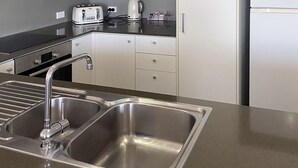 A modern kitchen with stainless steel appliances, a double sink, and black cabinets. - Curtis Central Apartments (Gladstone)