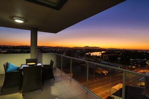 A balcony with wicker furniture and a view of a cityscape at dusk. - Curtis Central Apartments (Gladstone)