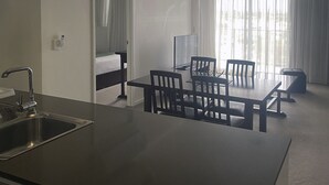 A modern hotel room with a kitchenette, a dining area with a table and chairs, a bed, and large windows with sheer curtains. - Curtis Central Apartments (Gladstone)