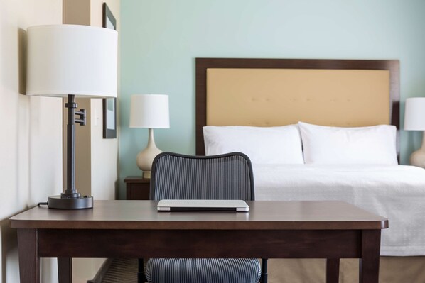 A hotel room with a bed, a desk with a laptop, a chair, and two bedside lamps.