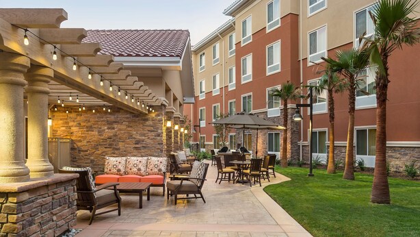 An outdoor patio area with stone columns, a stone wall, and a seating area with a sofa and chairs. - Homewood Suites By Hilton San Bernardino (San Bernardino)