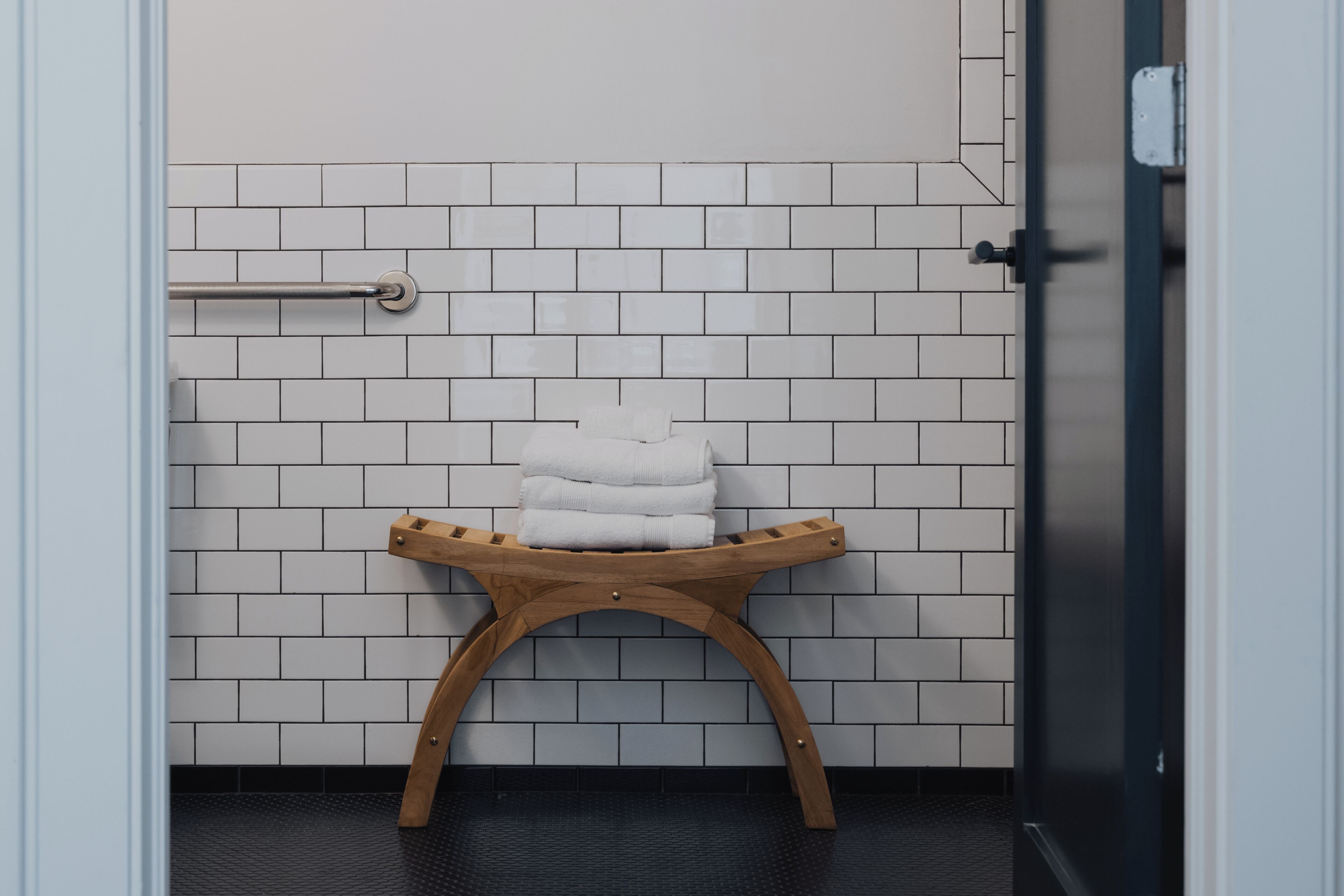 Ein Badezimmer mit weißen Fliesen, einem hölzernen Handtuchhalter und einem dunklen Boden.