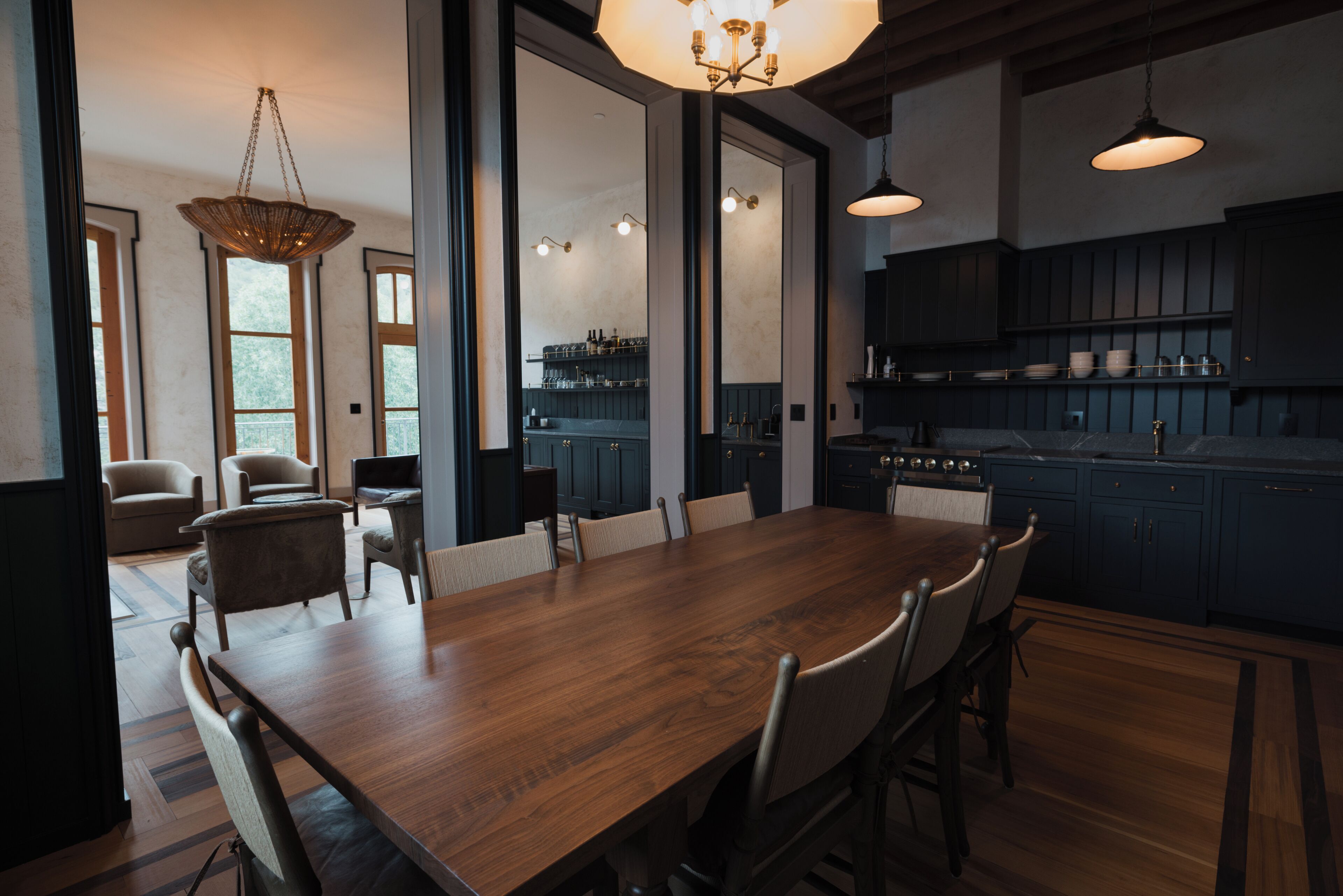 A modern kitchen with dark cabinetry, a wooden dining table, and pendant lighting.