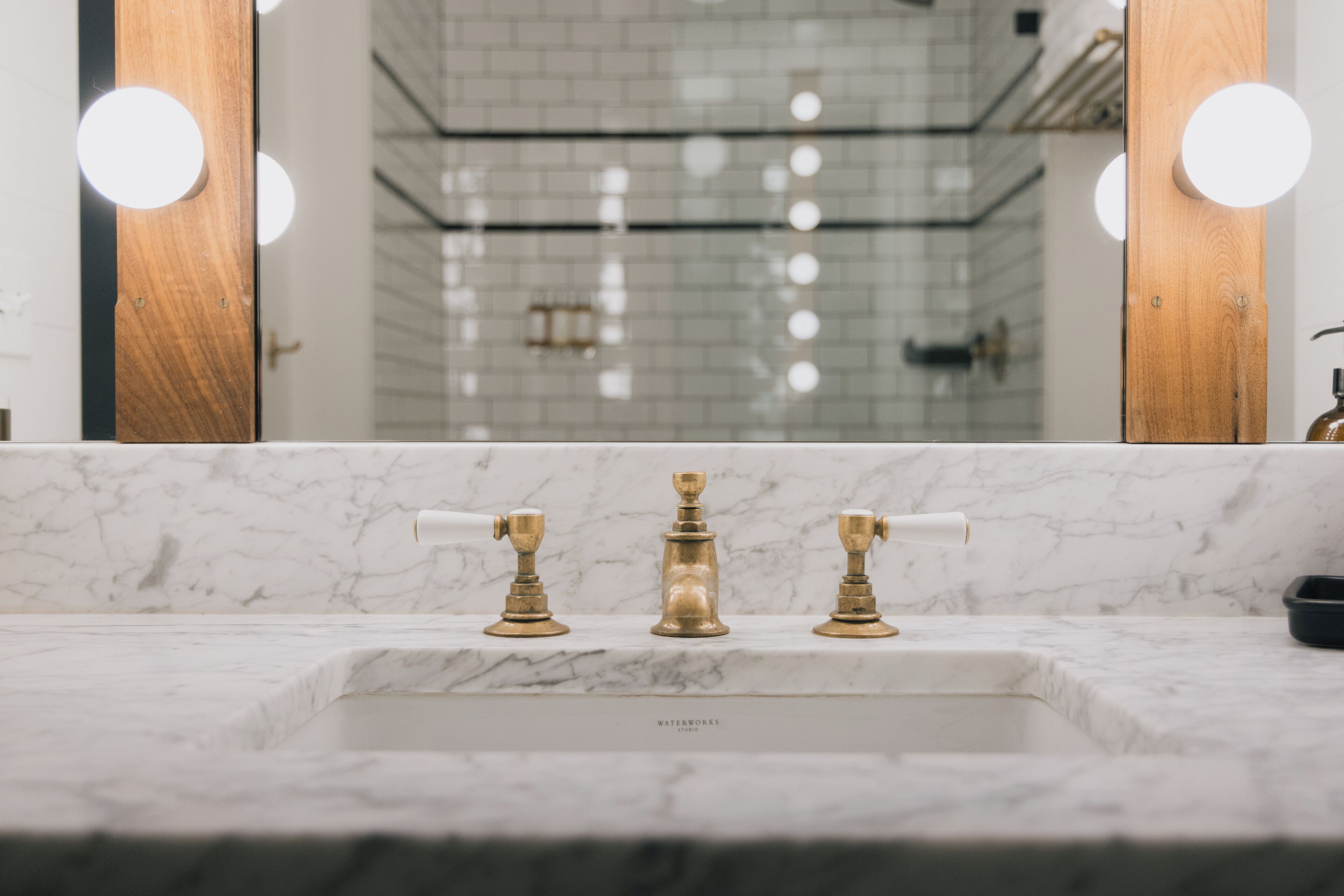 A bathroom with a marble sink, gold faucets, and a mirror with round lights.