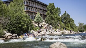 Hotel de vários andares com varandas, rodeado por árvores e um rio.