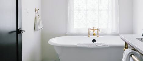 A bathroom with a freestanding bathtub, a window with sheer curtains, a towel rack, and a marble floor.
