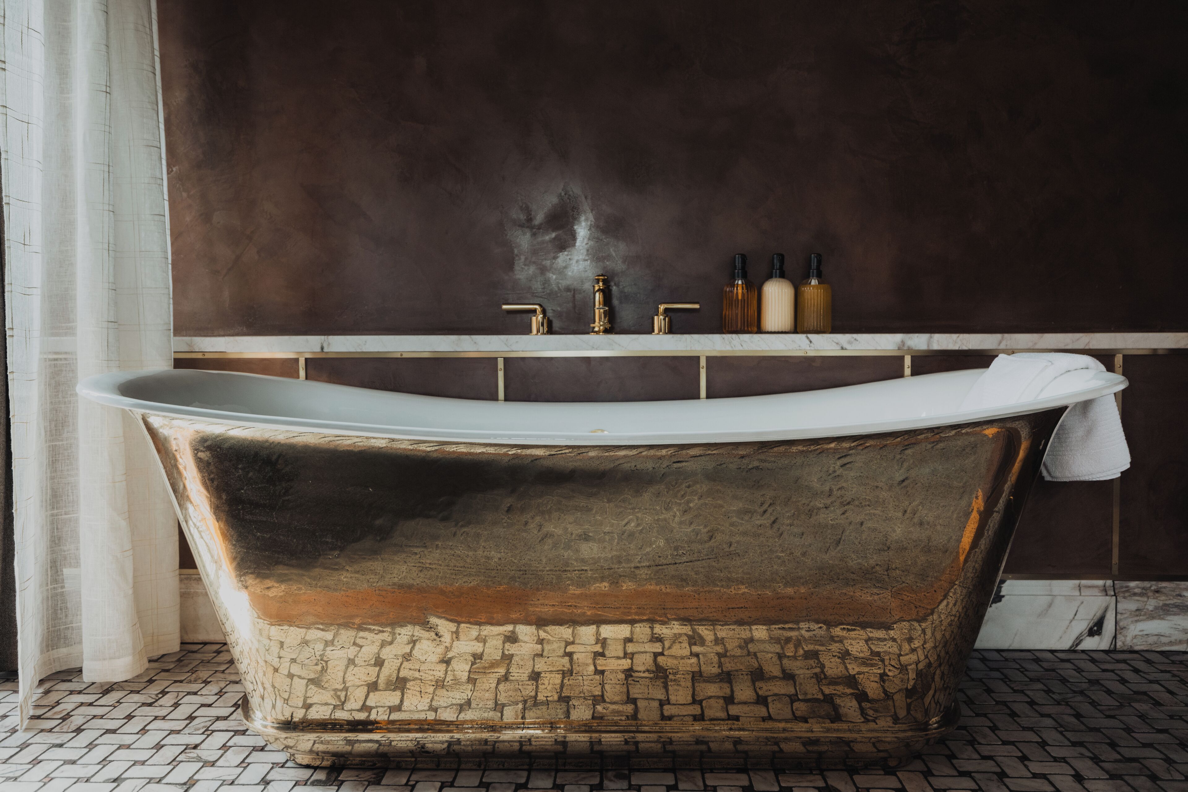 Una bañera independiente en un baño con pared oscura y suelo de baldosas.