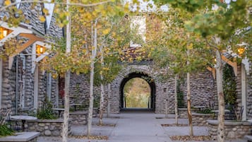 An outdoor pathway leading through a stone archway, flanked by trees and benches, suggesting a tranquil garden or courtyard setting.