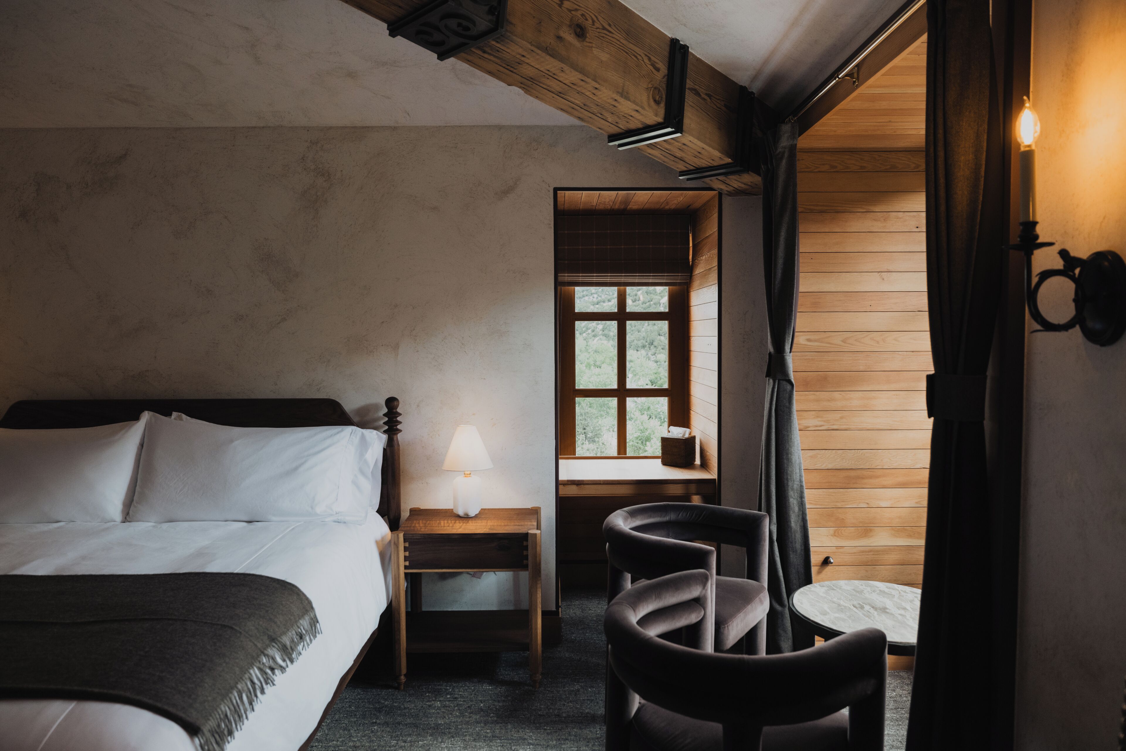 Ein Schlafzimmer mit Bett, Nachttisch, Lampe und Blick ins Freie durch ein Fenster.