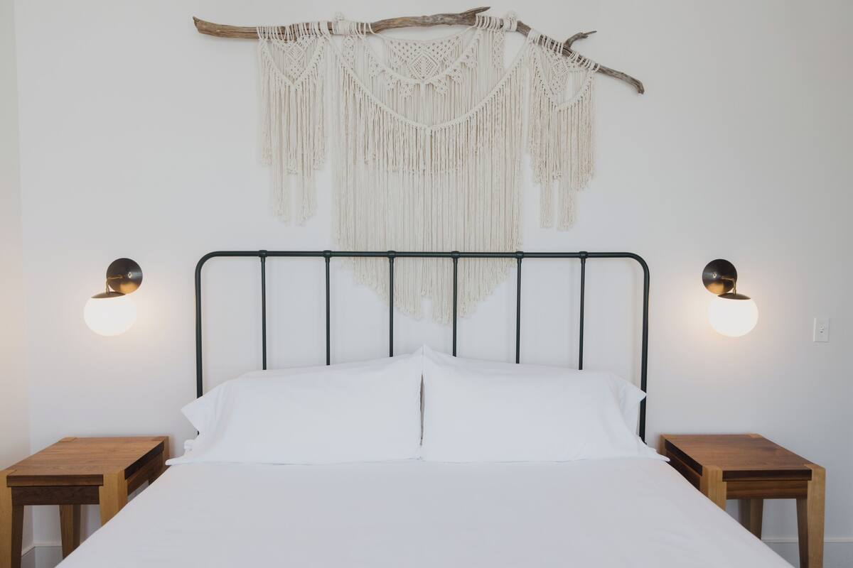 Een bed met hoofdbord, twee nachtkastjes, macramewanddecoratie en wandlampen.