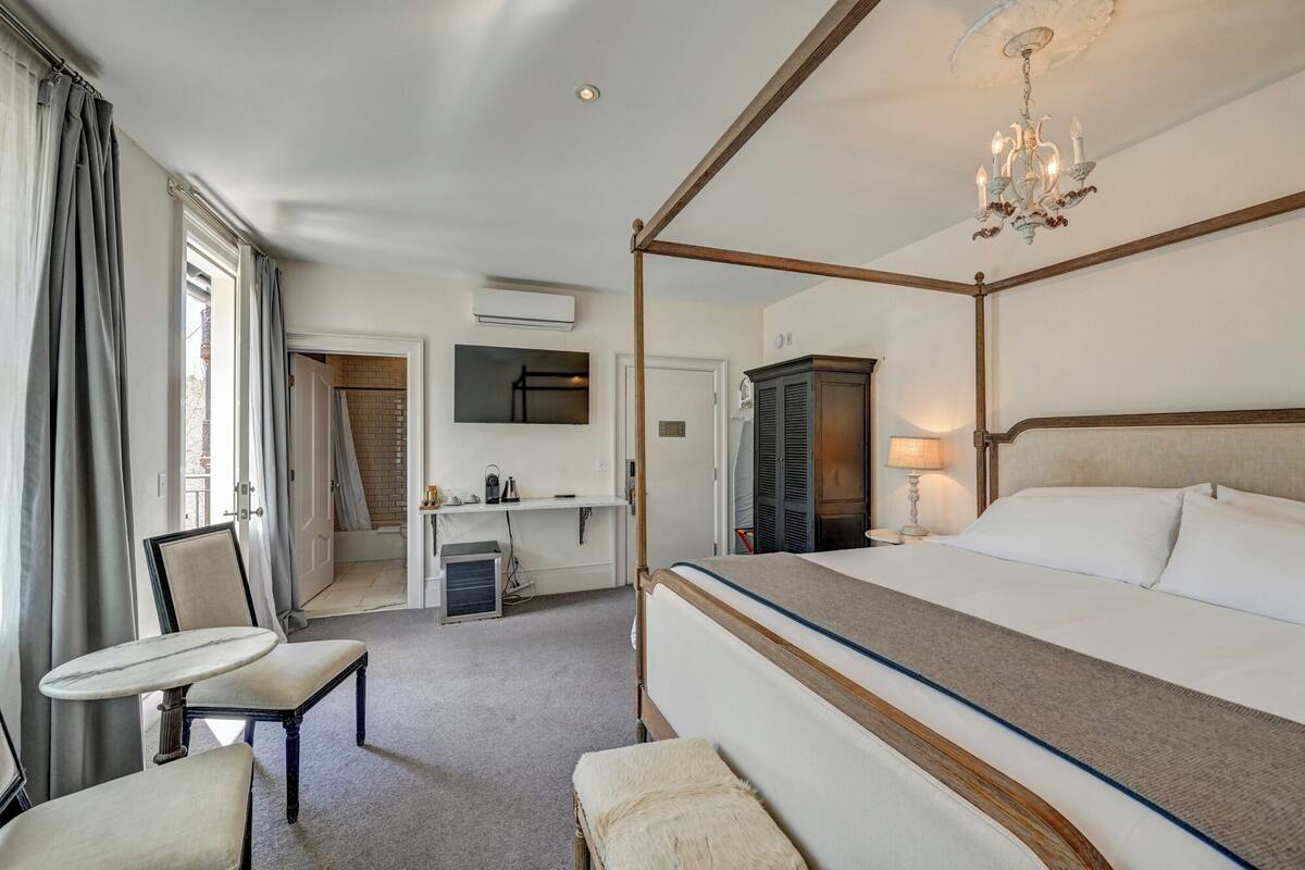 Een hemelbed, een bureau met stoel, een kledingkast en een kroonluchter in een hotelkamer.
