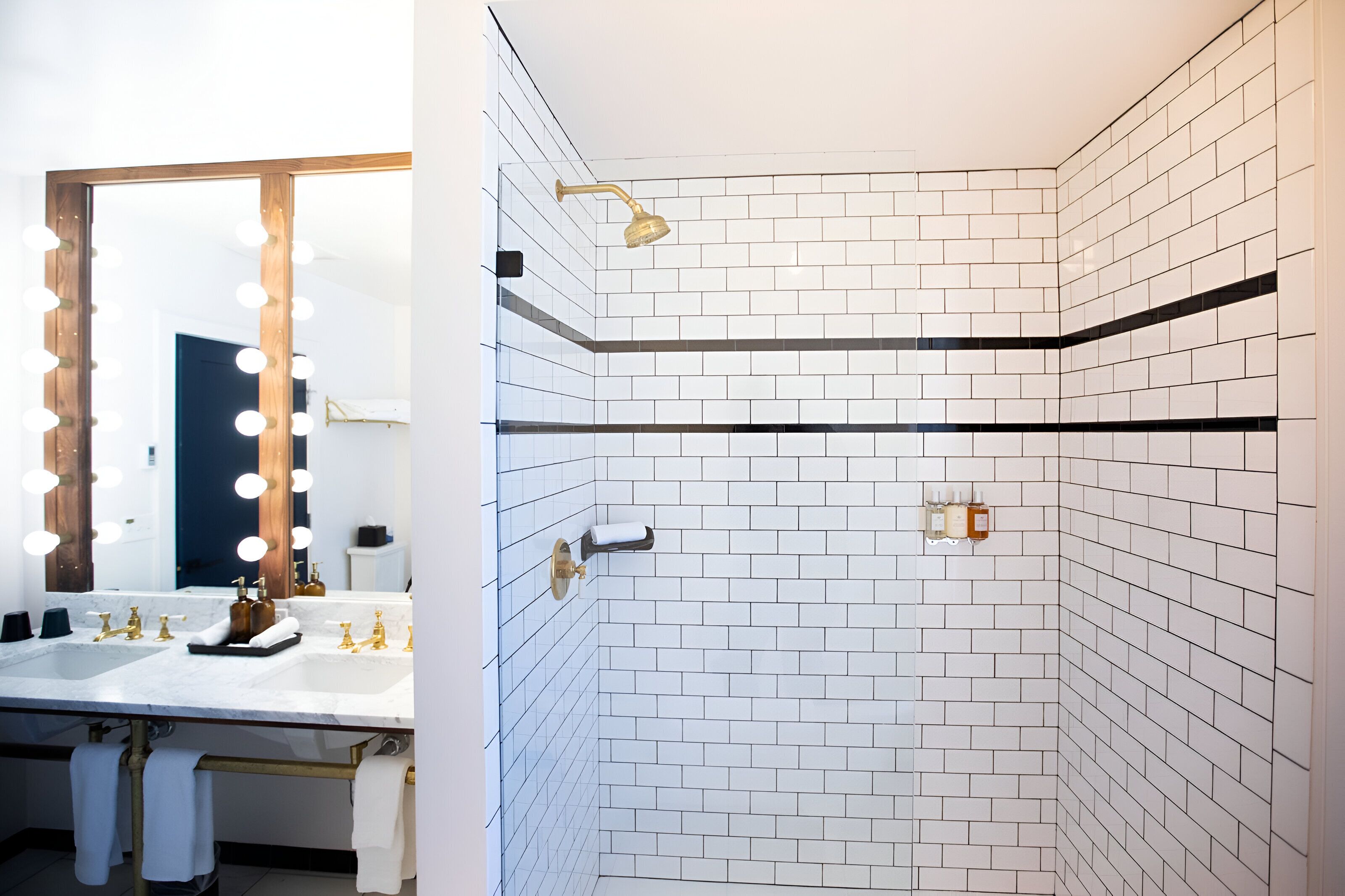 A bathroom with a large mirror, vanity, and a shower area with white tiled walls and a black accent strip.