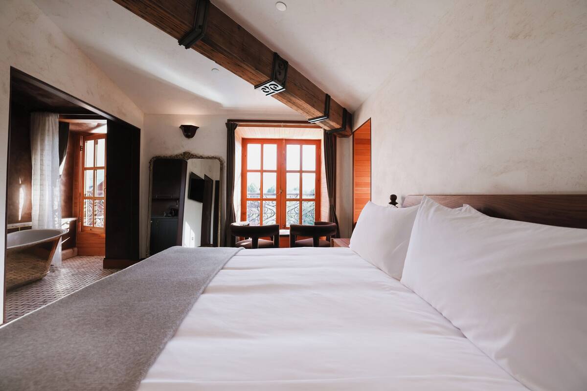 Een slaapkamer met een groot bed, houten balken, een raam en een bankje.