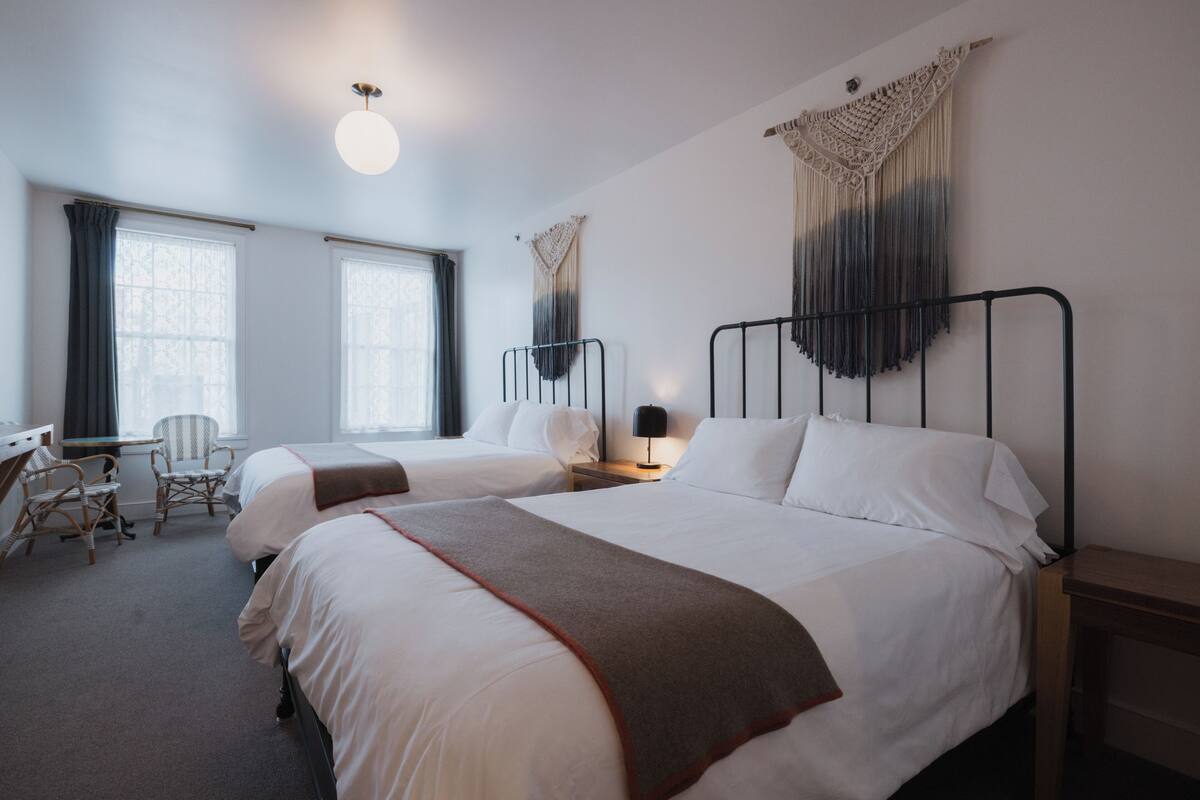 Een hotelkamer met twee bedden, een bureau, een stoel en een wandtapijt van macramé.
