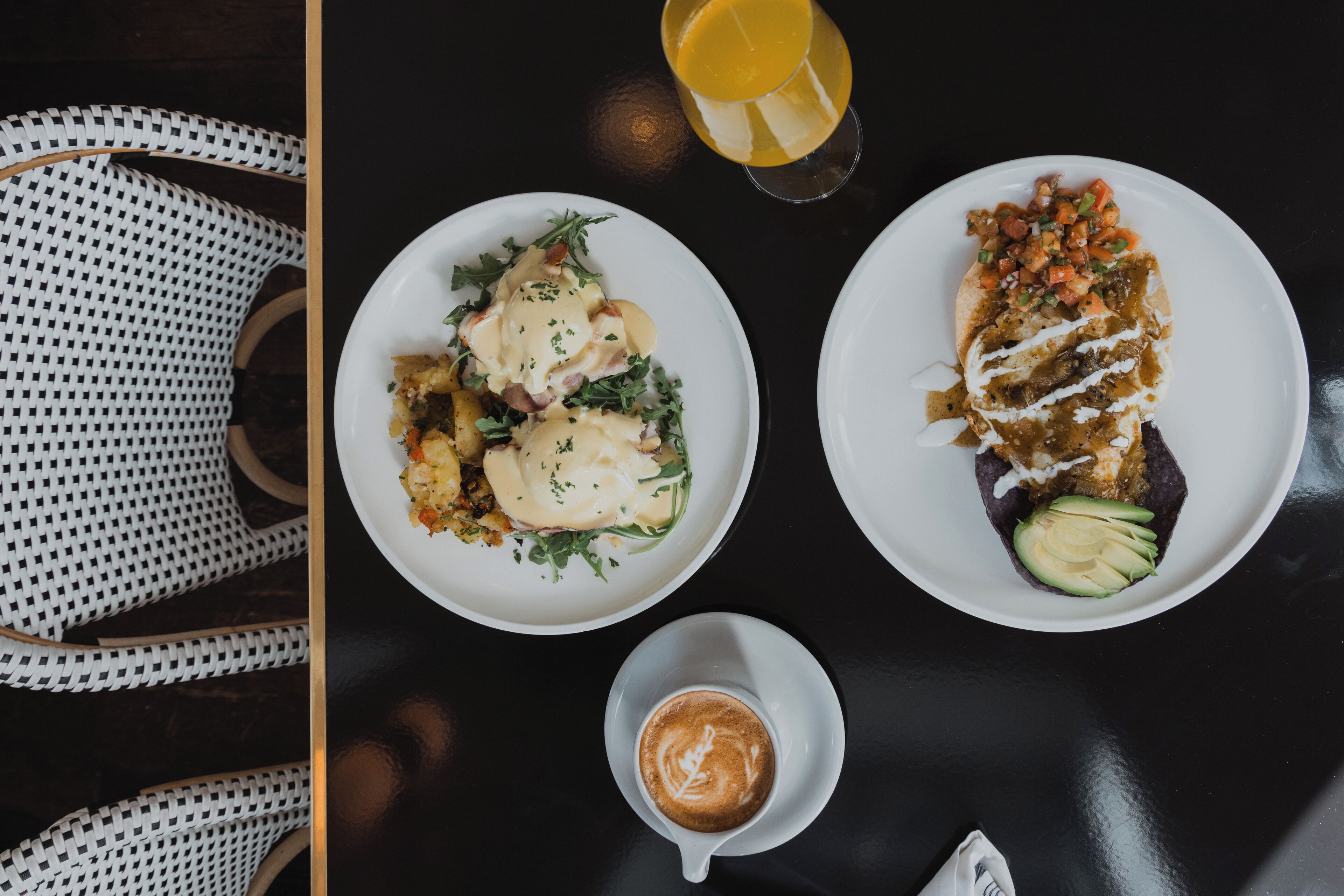 A dining table with two plates of food, a glass of orange juice, and a cup of coffee.