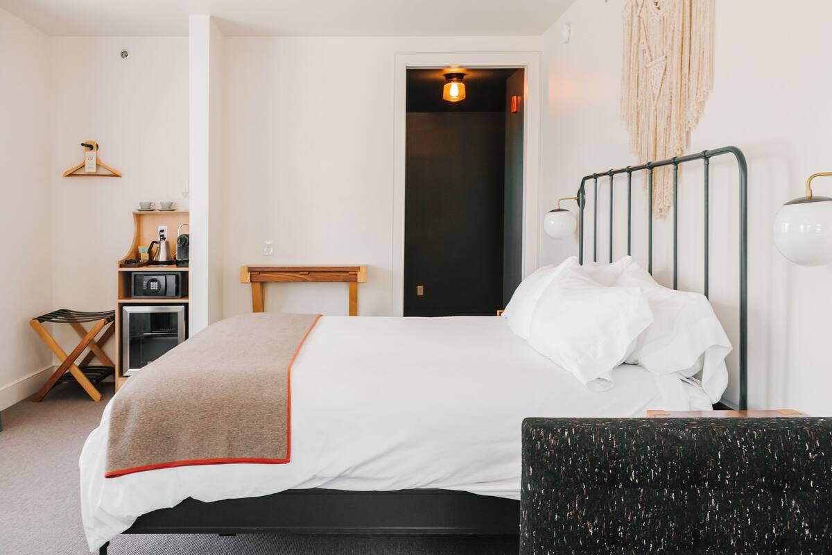 Een netjes ingerichte hotelkamer met een bed, nachtkastje en een klein bureau met stoel.