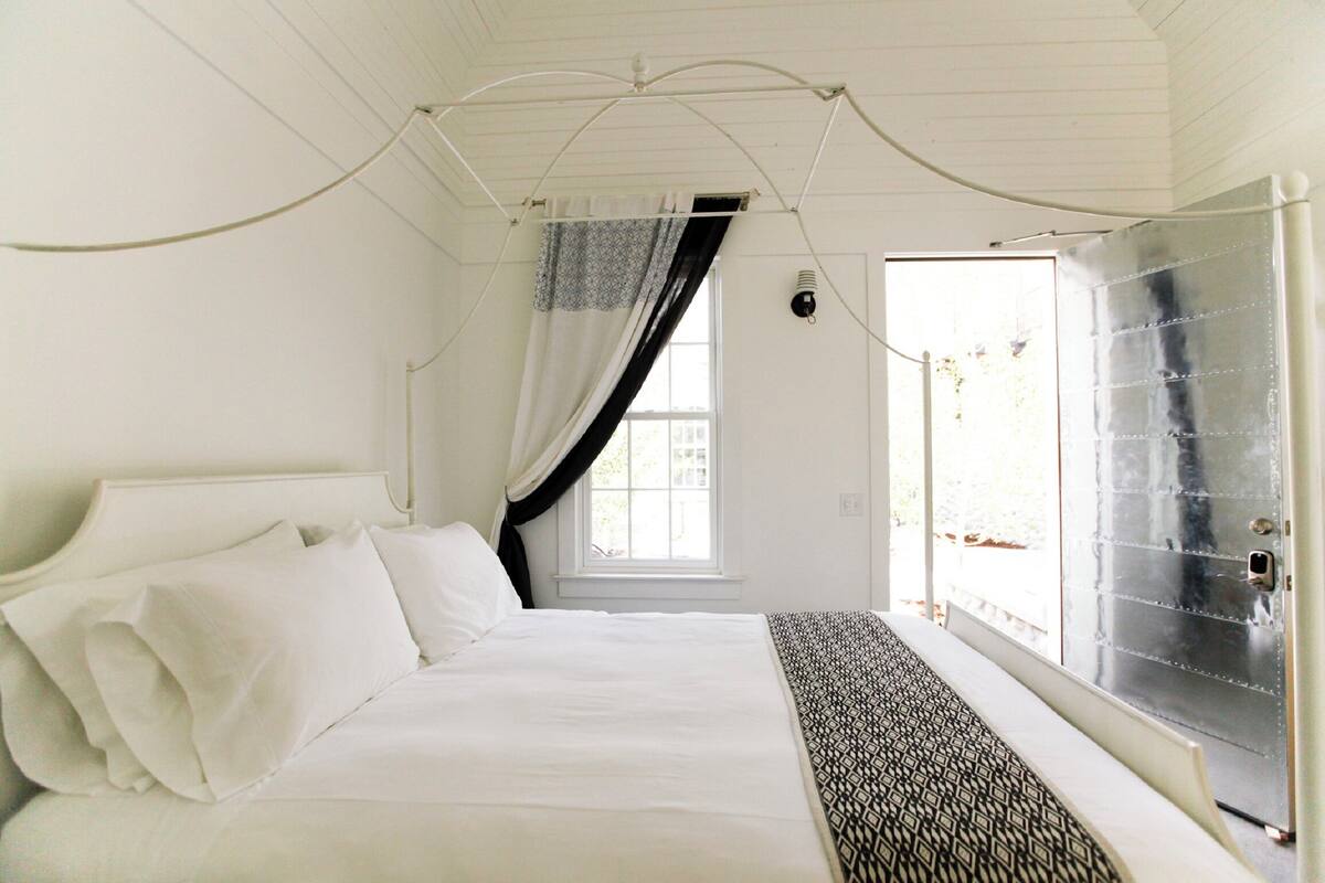 Een slaapkamer met een bed, een raam met gordijnen en een deur met een metalen paneel.