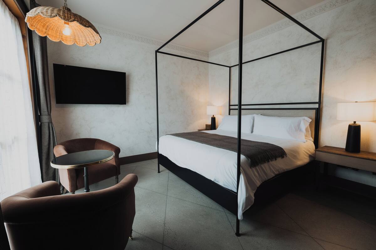 Een bed met baldakijn, een hoofdbord, een ronde tafel, een stoel en een aan de muur bevestigde televisie.