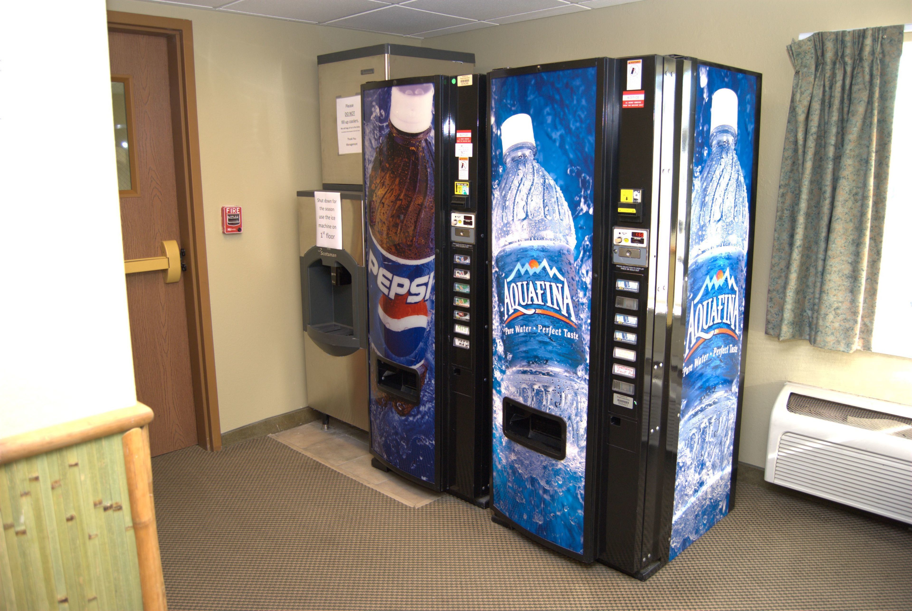Una fila di distributori automatici con bevande Pepsi e acqua Aquafina in un corridoio.