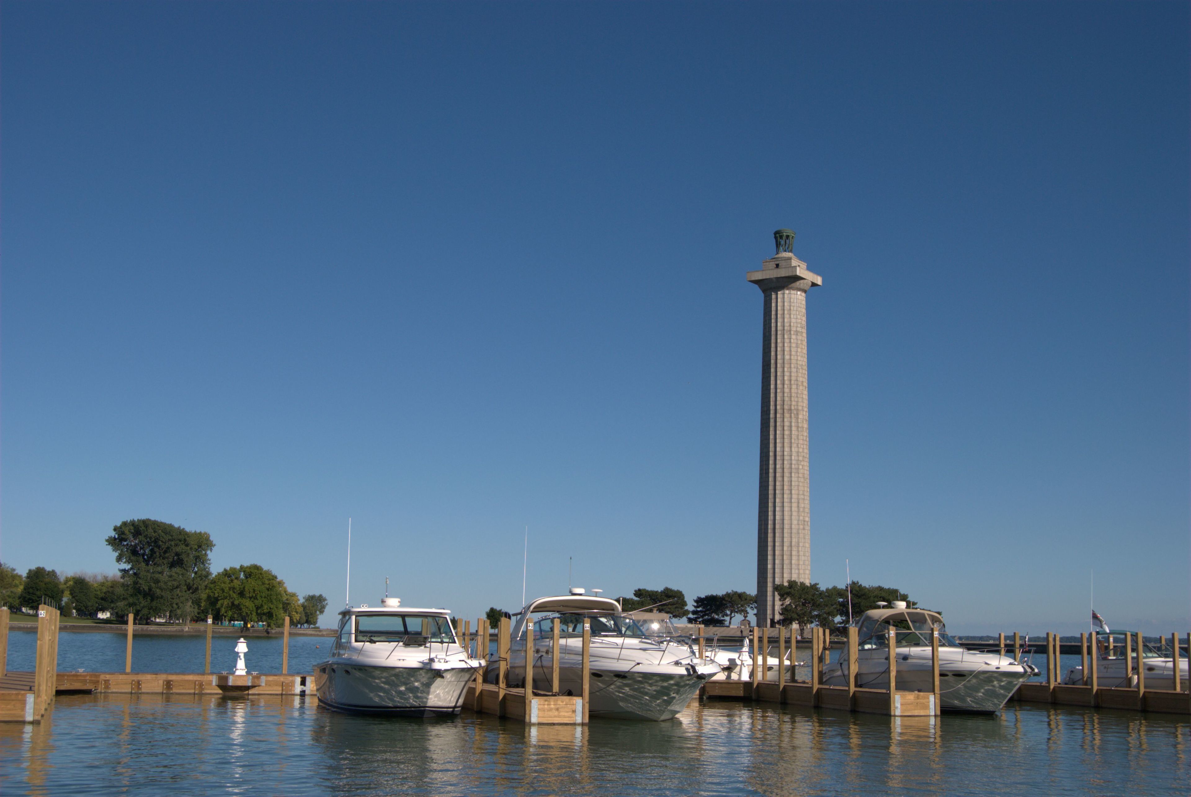 Un port de plaisance avec plusieurs bateaux amarrés, une haute tour et un ciel bleu dégagé.