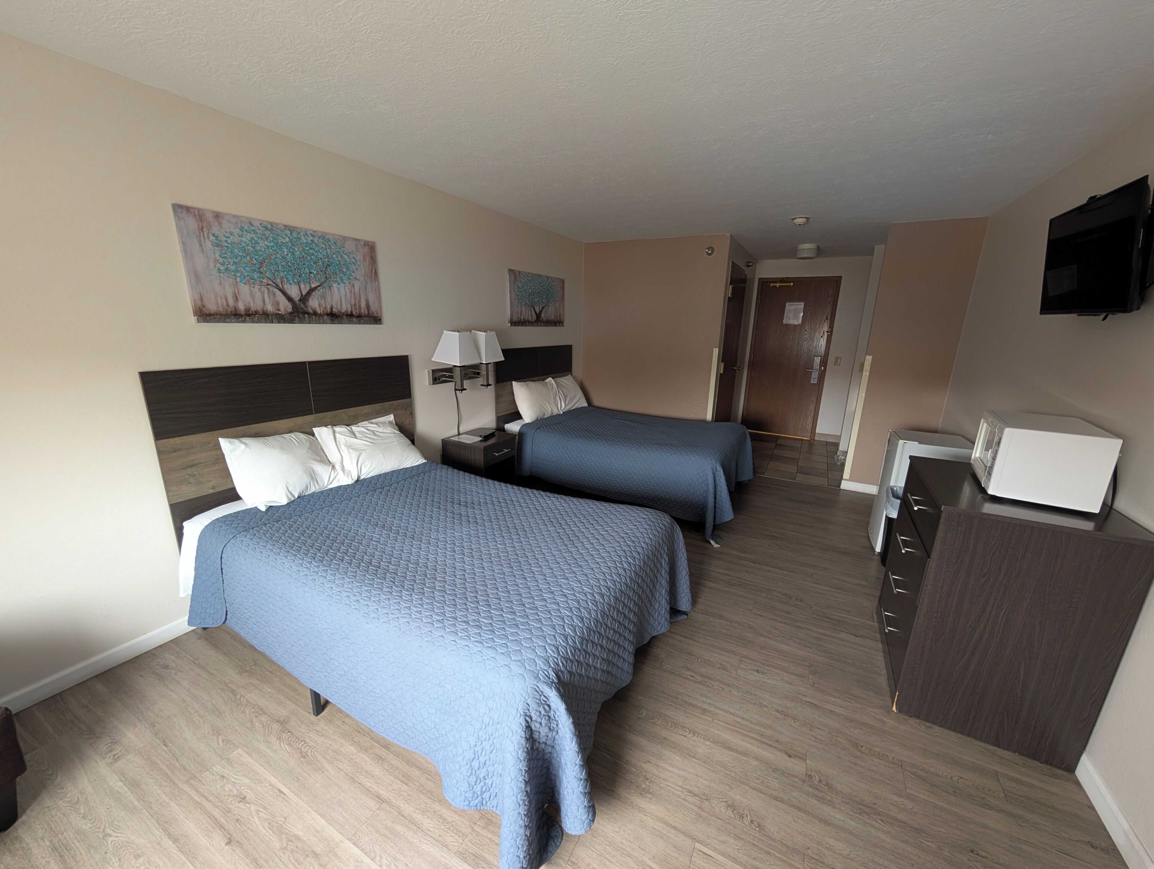 A hotel room with two beds, a desk, a TV, and artwork on the walls.