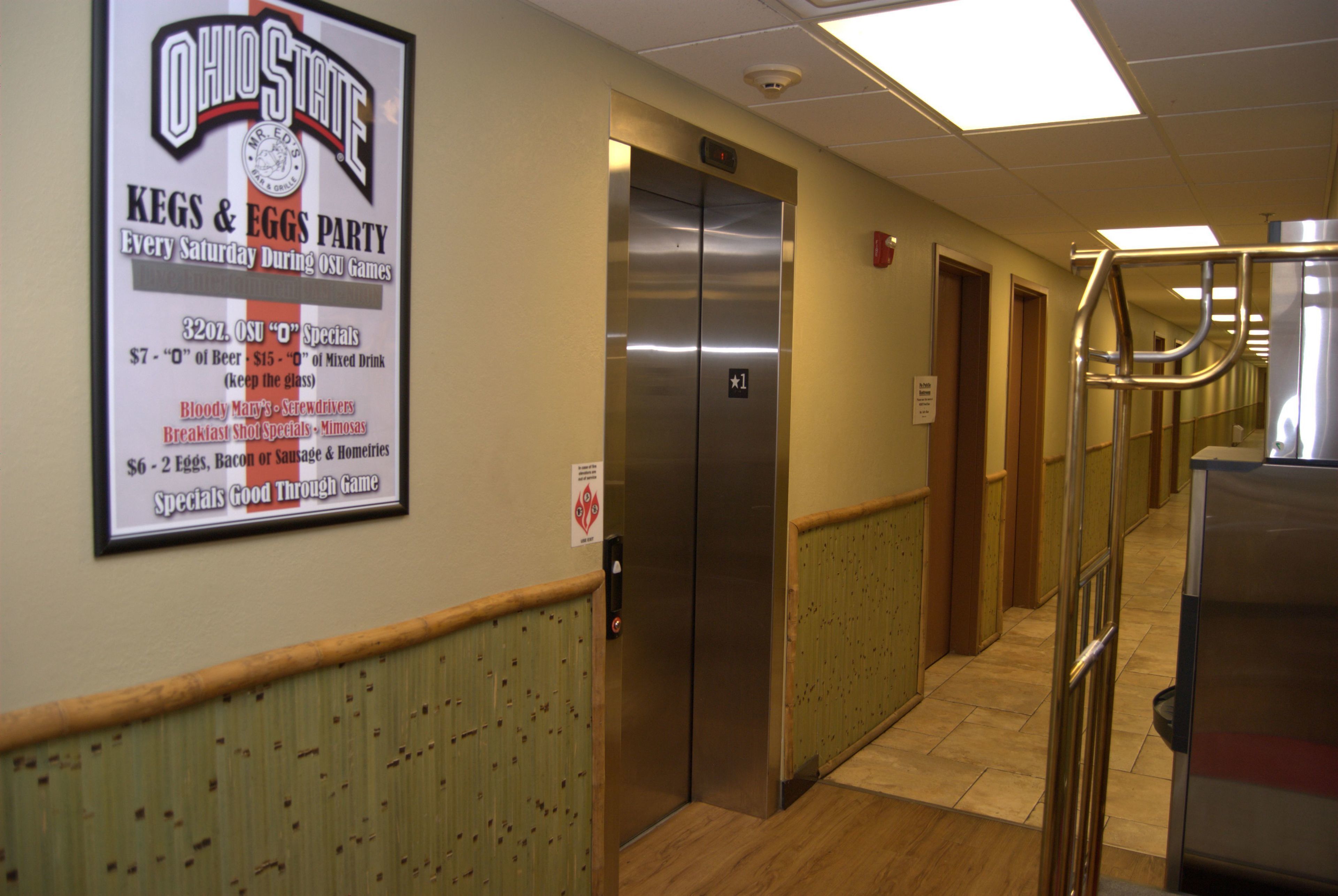 A hallway with a sign for Ohio State's Kegs & Eggs Party, an elevator, and a trash can.