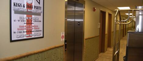 A hallway with a sign for Ohio State's Kegs & Eggs Party, an elevator, and a trash can.