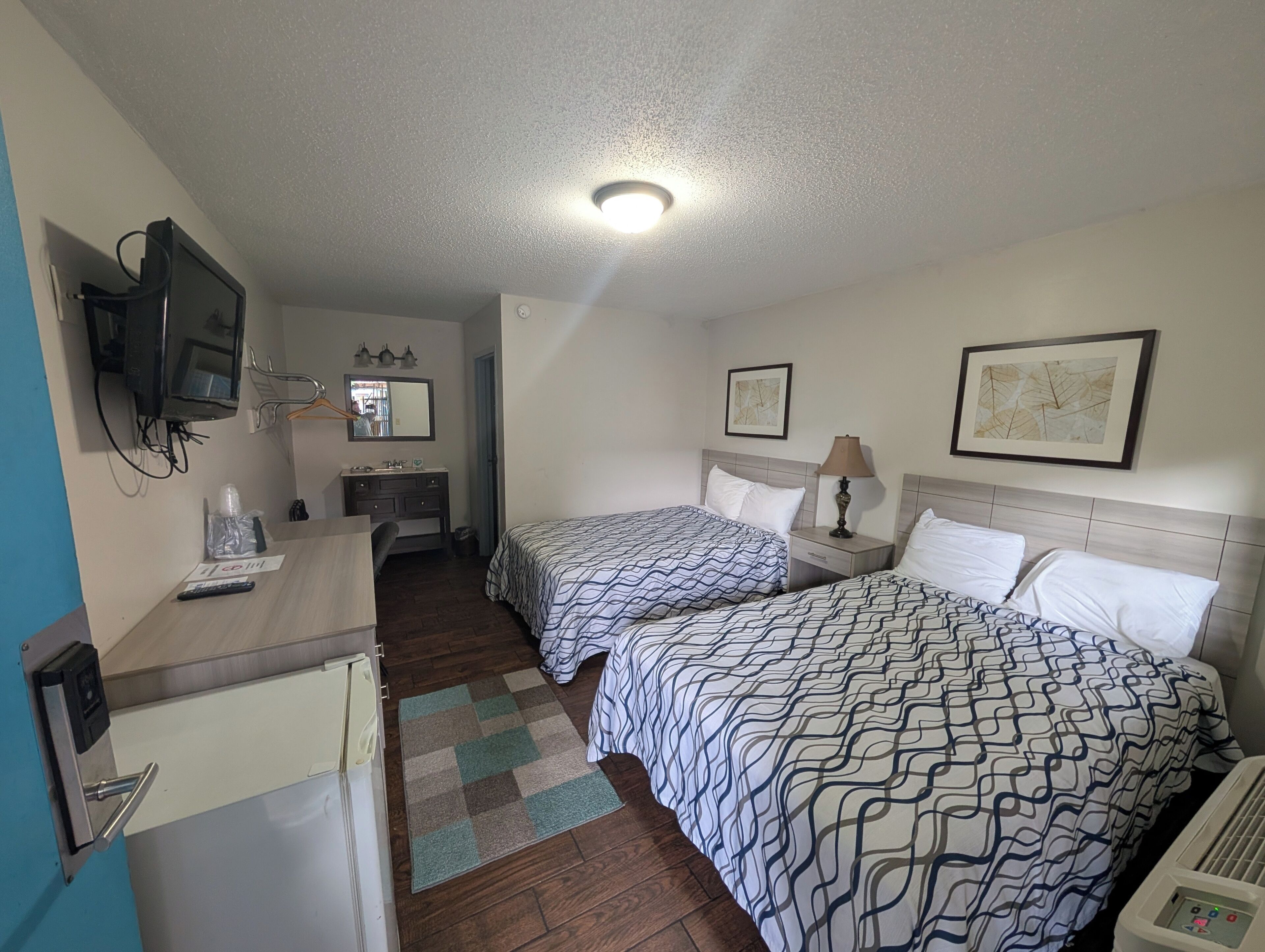 Habitación de hotel con dos camas, un escritorio, televisor y una kitchenette pequeña.