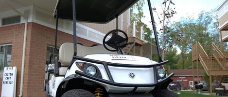 A golf cart parked in front of a building with a sign for custom cart rentals.