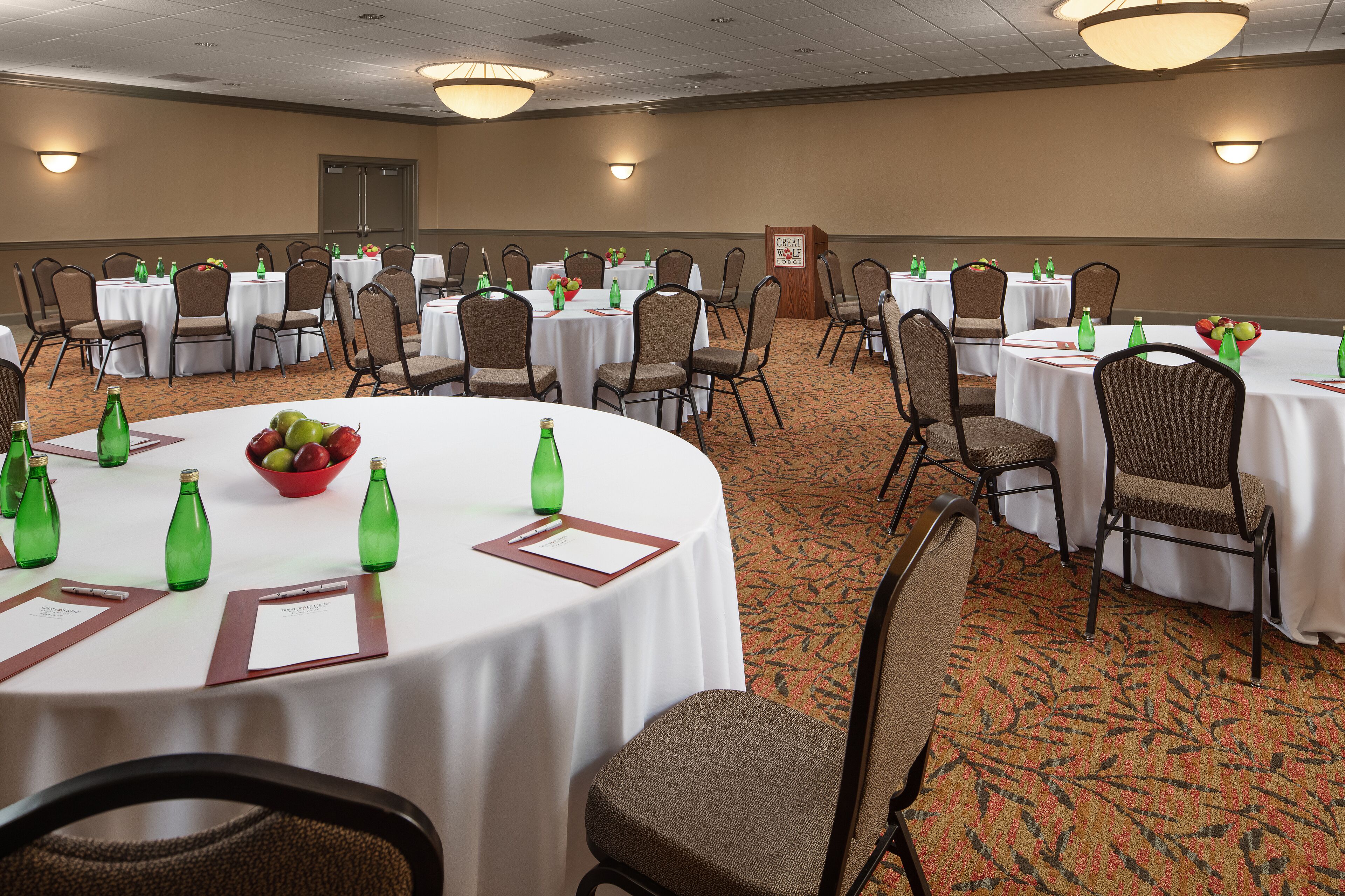 A conference room with multiple tables, chairs, and green bottles.