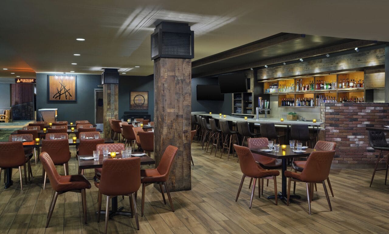 Ein Restaurant mit Holzboden, braunen Polstersesseln und einer Bar mit Flaschenregalen.