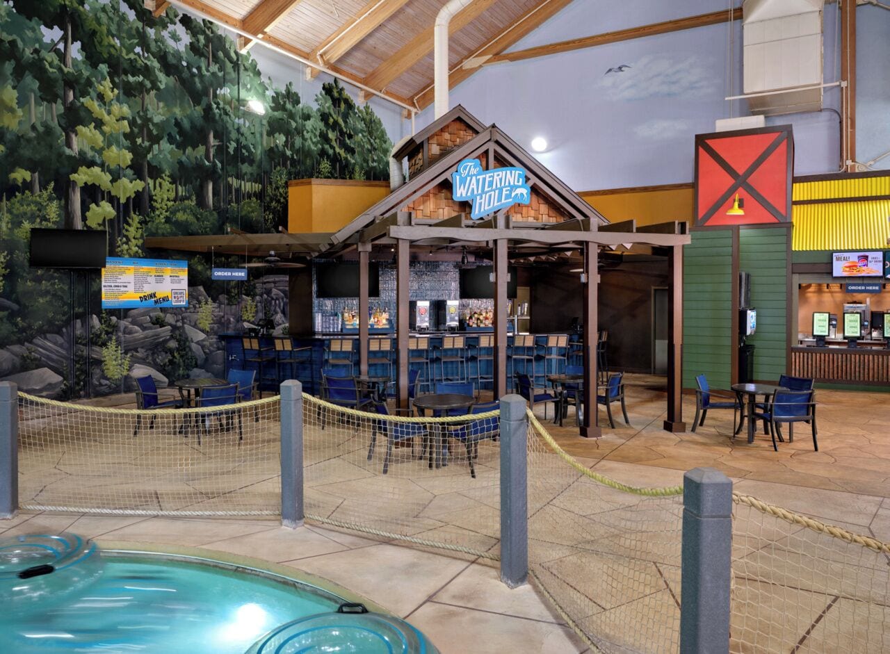An indoor recreational area with a pool, seating, and a bar area labeled 'The Watering Hole.'