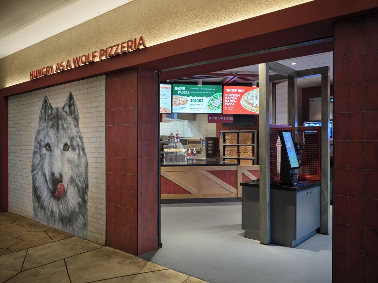 Un restaurante de pizzas con un mural de lobo y una pantalla digital para el menú.