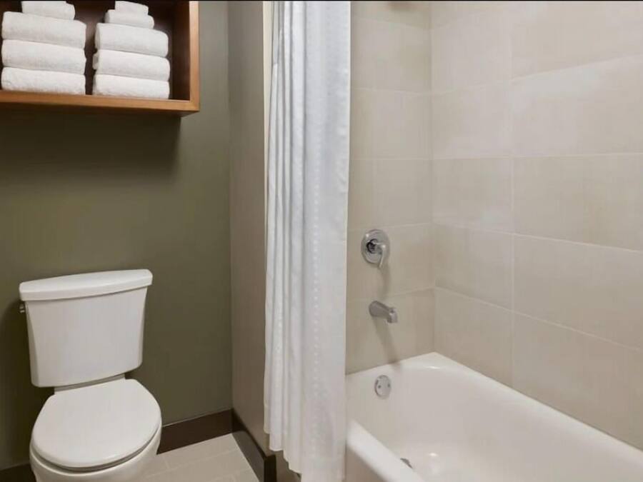 A bathroom with a toilet, a bathtub, and a shelf with folded towels.
