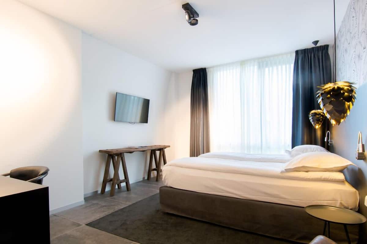 Quarto de hotel moderno com uma cama grande, uma escrivaninha, uma cadeira e uma televisão na parede.