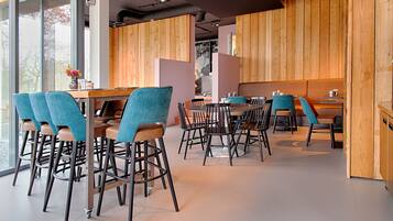 Un comedor moderno con paneles de madera, una combinación de asientos tipo barra y cabinas, y un amplio ventanal que proporciona luz natural.