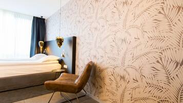 A modern hotel room with a large bed, a wooden headboard, a brown leather chair, and a patterned wallpaper.