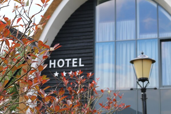 A hotel sign with "HOTEL" and stars, a lamp post, and autumn leaves in the foreground.