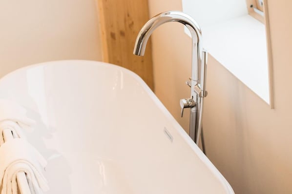 Un baño moderno con una bañera independiente, un grifo cromado y una encimera blanca.