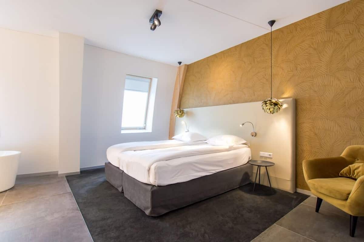 Um quarto moderno com uma cama, mesa de cabeceira, abajur e uma cadeira.