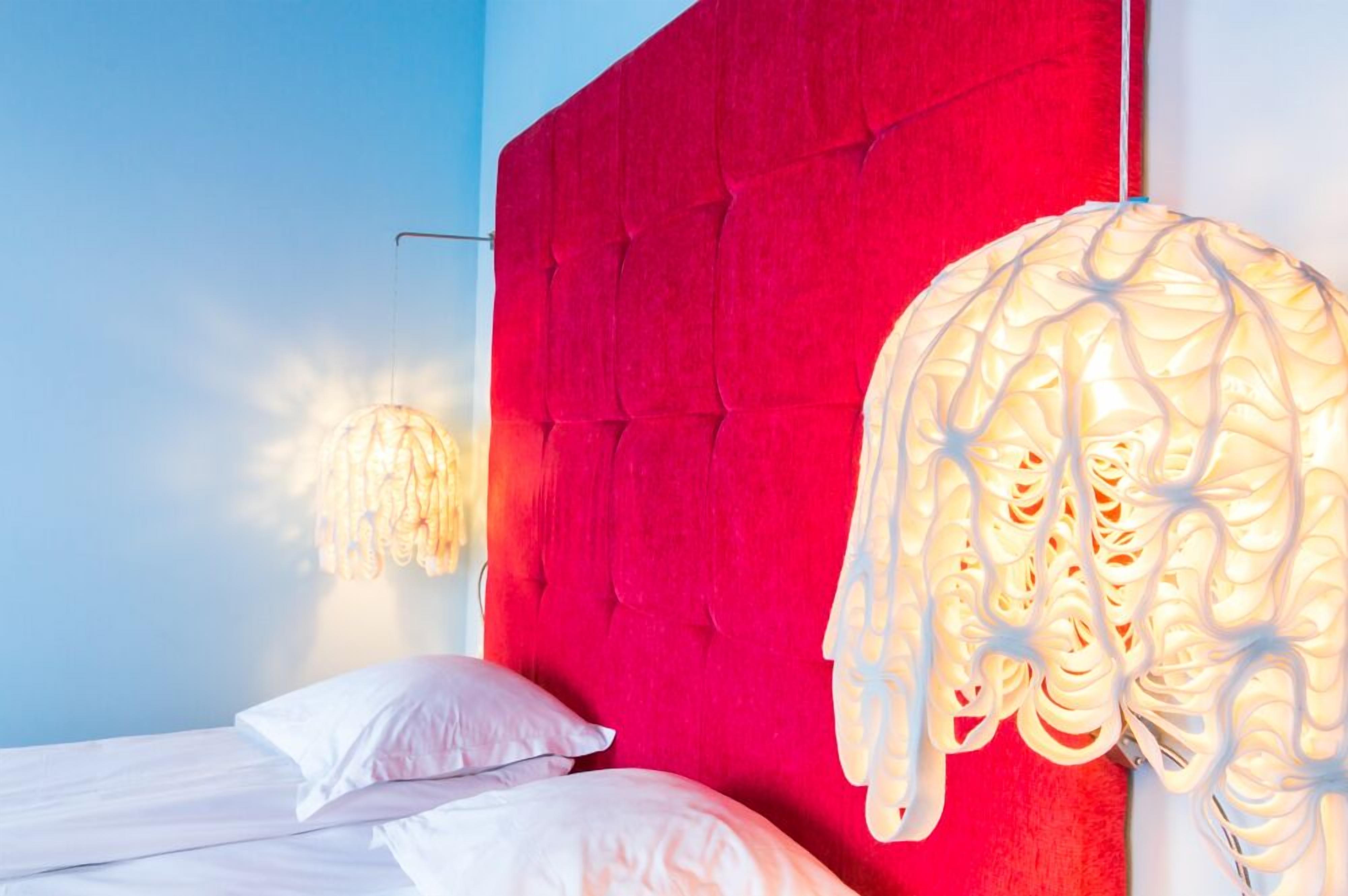 Een slaapkamer met een rood hoofdeinde, een bed met witte beddengoed en een hanglamp.