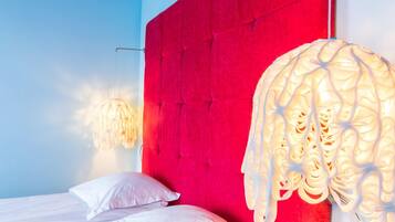 Een slaapkamer met een rood hoofdeinde, een bed met witte beddengoed en een hanglamp.