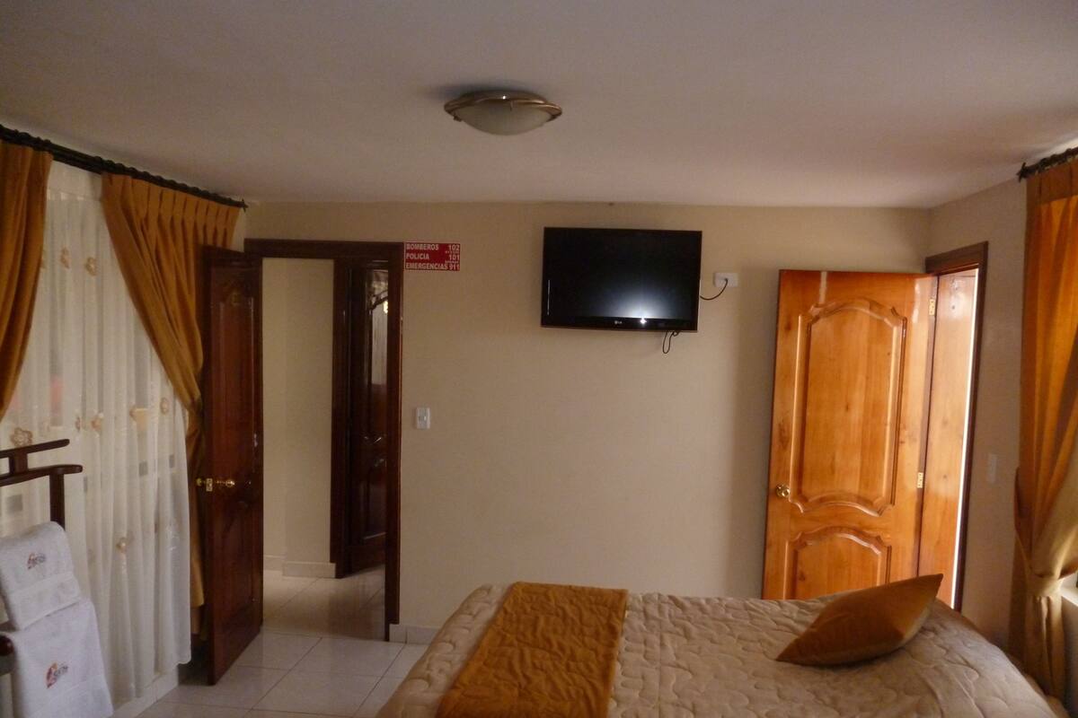 A hotel room with a bed, a television mounted on the wall, and a wooden door.