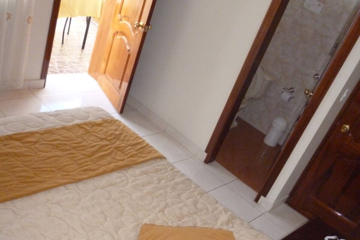 A hotel room with a bed, a bedside table with a phone, and a bathroom visible through an open door.