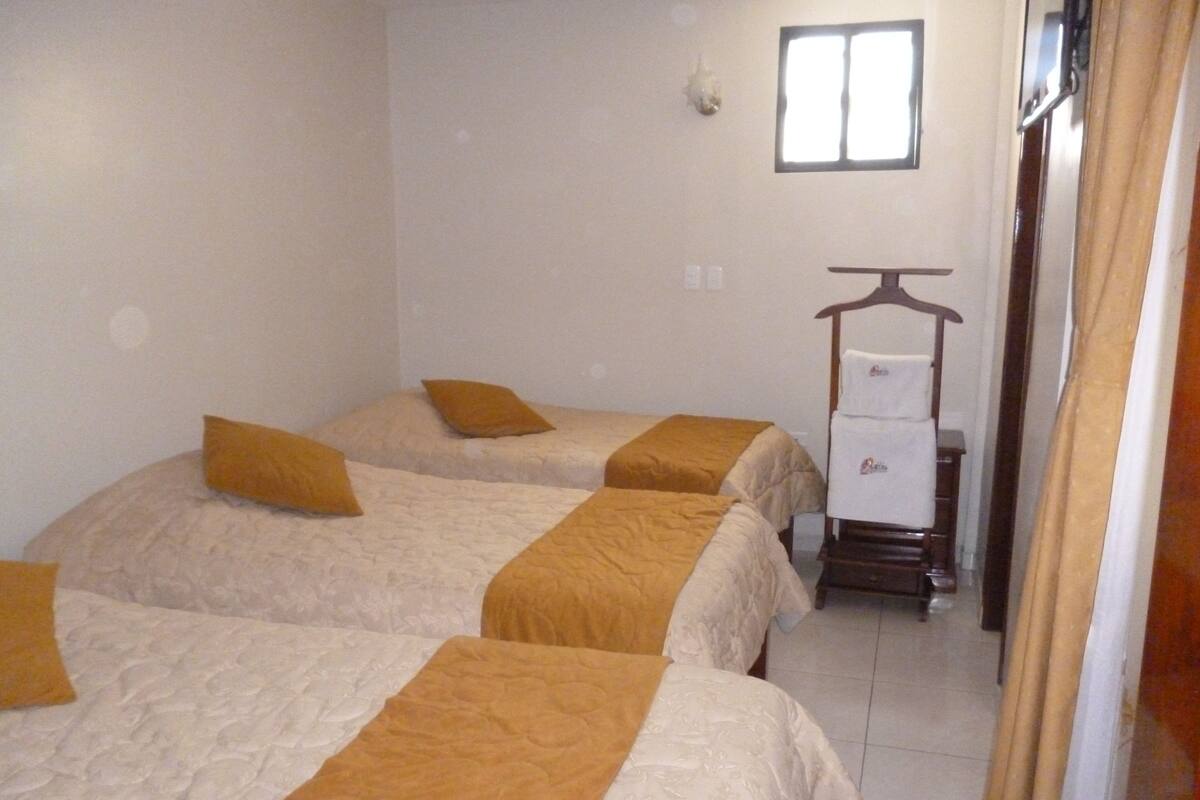 A hotel room with two beds, each with a brown bedspread and pillows. There is a small table with a chair and a coat rack with a coat hanging on it.