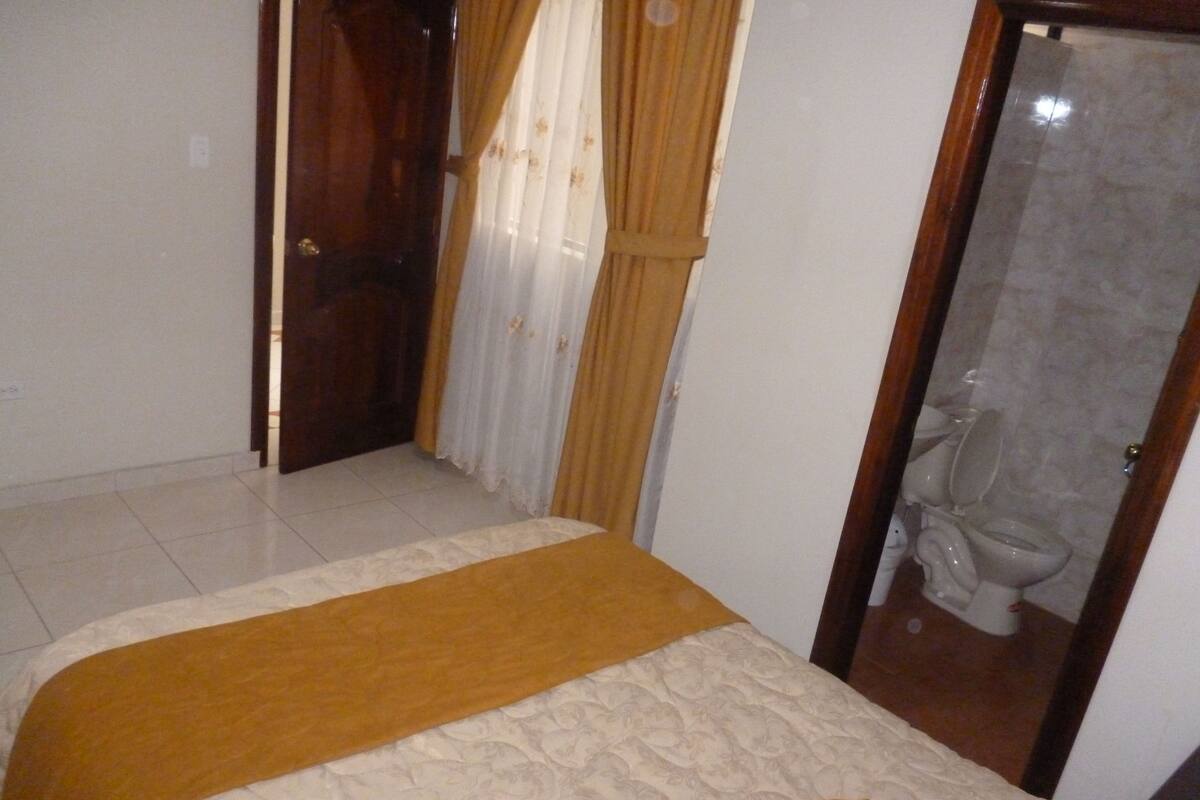 A bedroom with a bed, a wooden door, and a bathroom visible through a glass door.