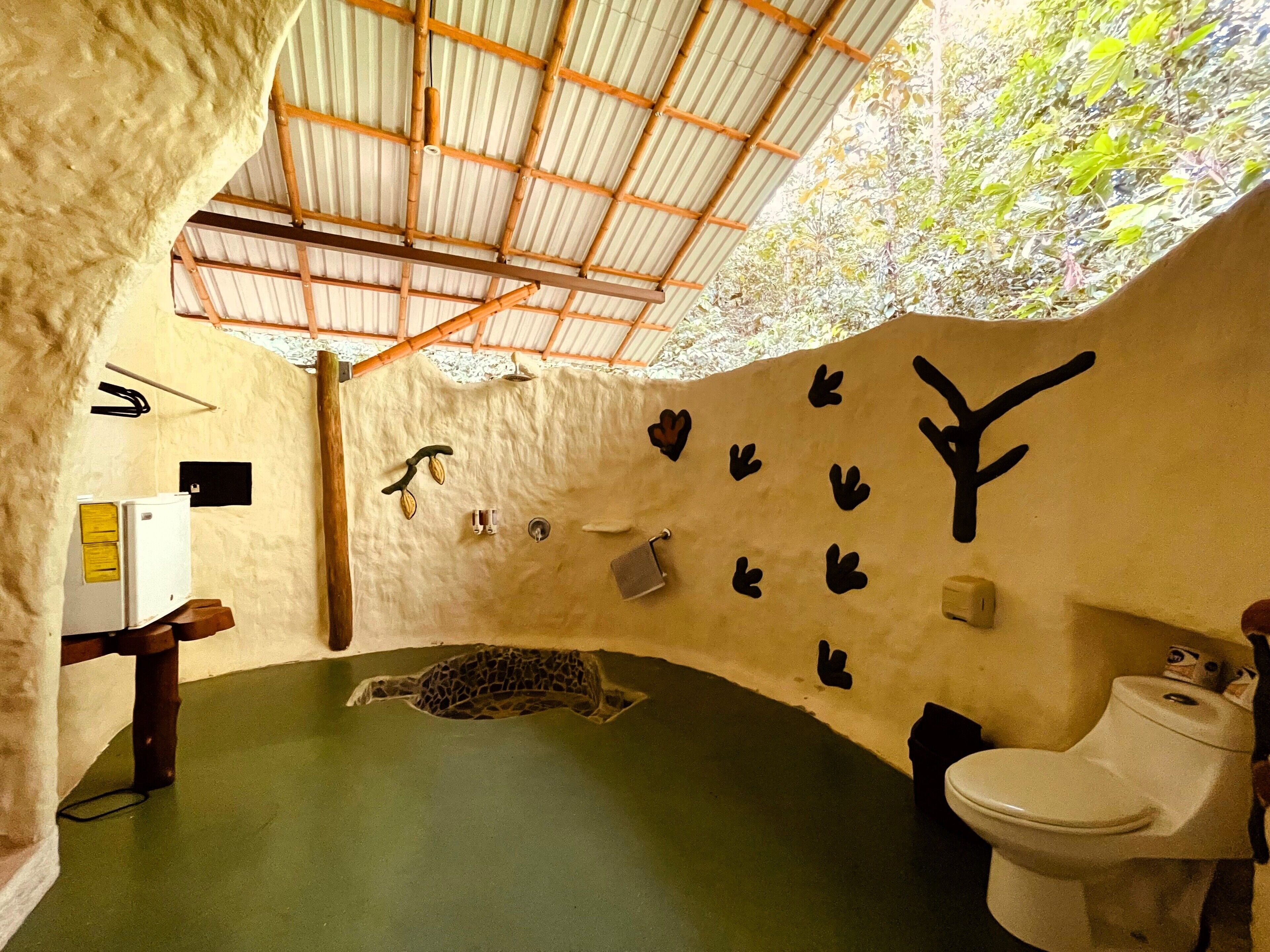 A room with a unique curved ceiling, a green floor, a toilet, and wall decorations including handprints and a tree branch.