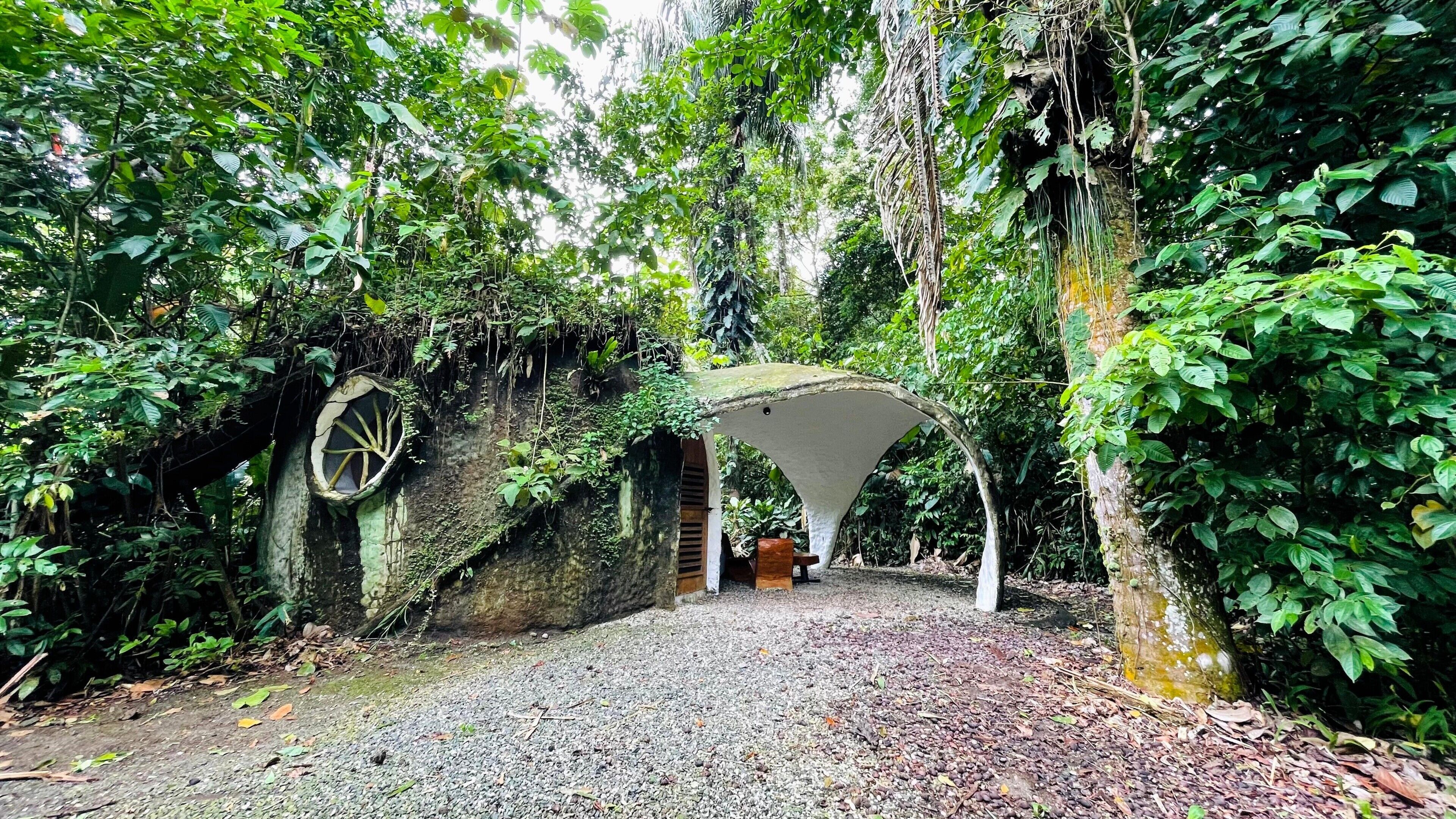 A natural stone archway leading into a forested area with a gravel path.