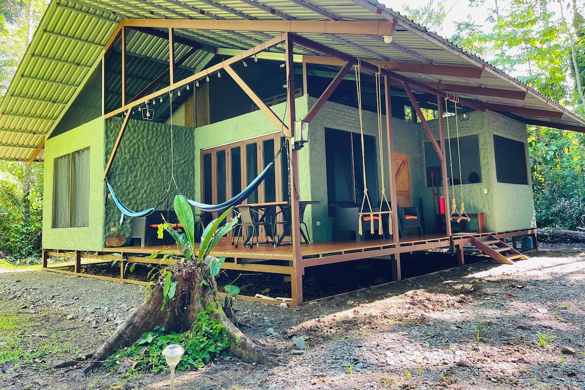 A rustic cabin with a porch, large windows, and a hammock.